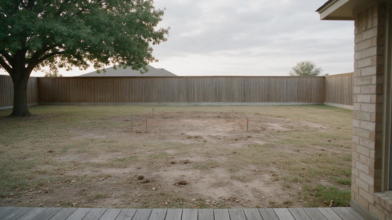 Empty backyard of a Bedford, Texas home before Limarti Group built the pool: bare dirt, stakes marking the pool footprint, and a wood privacy fence